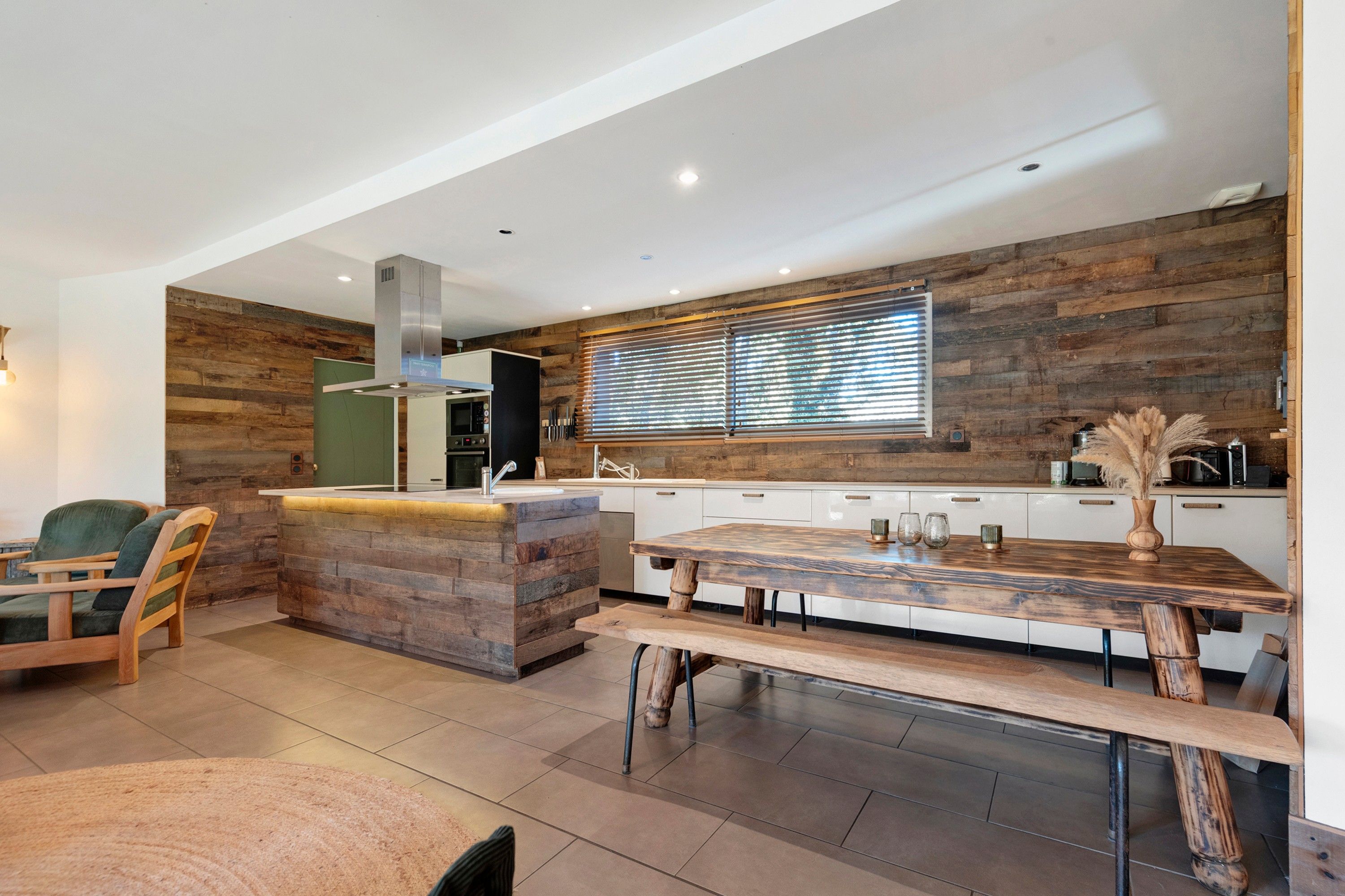 A modern kitchen with a wooden accent wall, a built-in oven, and a large window with blinds.
