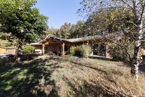 Une maison dotée d’un patio couvert, d’un coin repas et d’un grand arbre en premier plan.