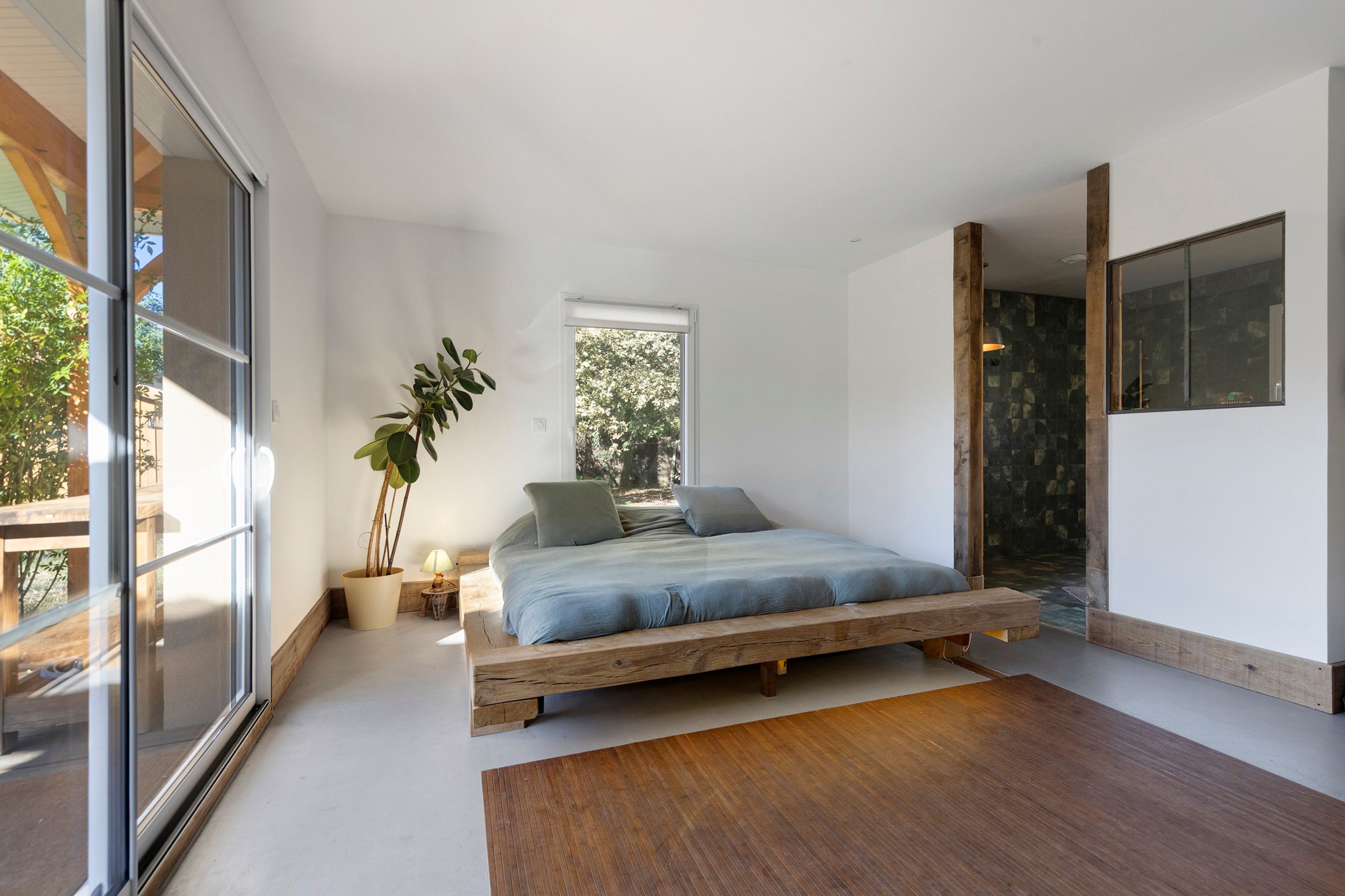 Une chambre moderne avec un grand lit, une plante en pot et une vue sur l’extérieur.