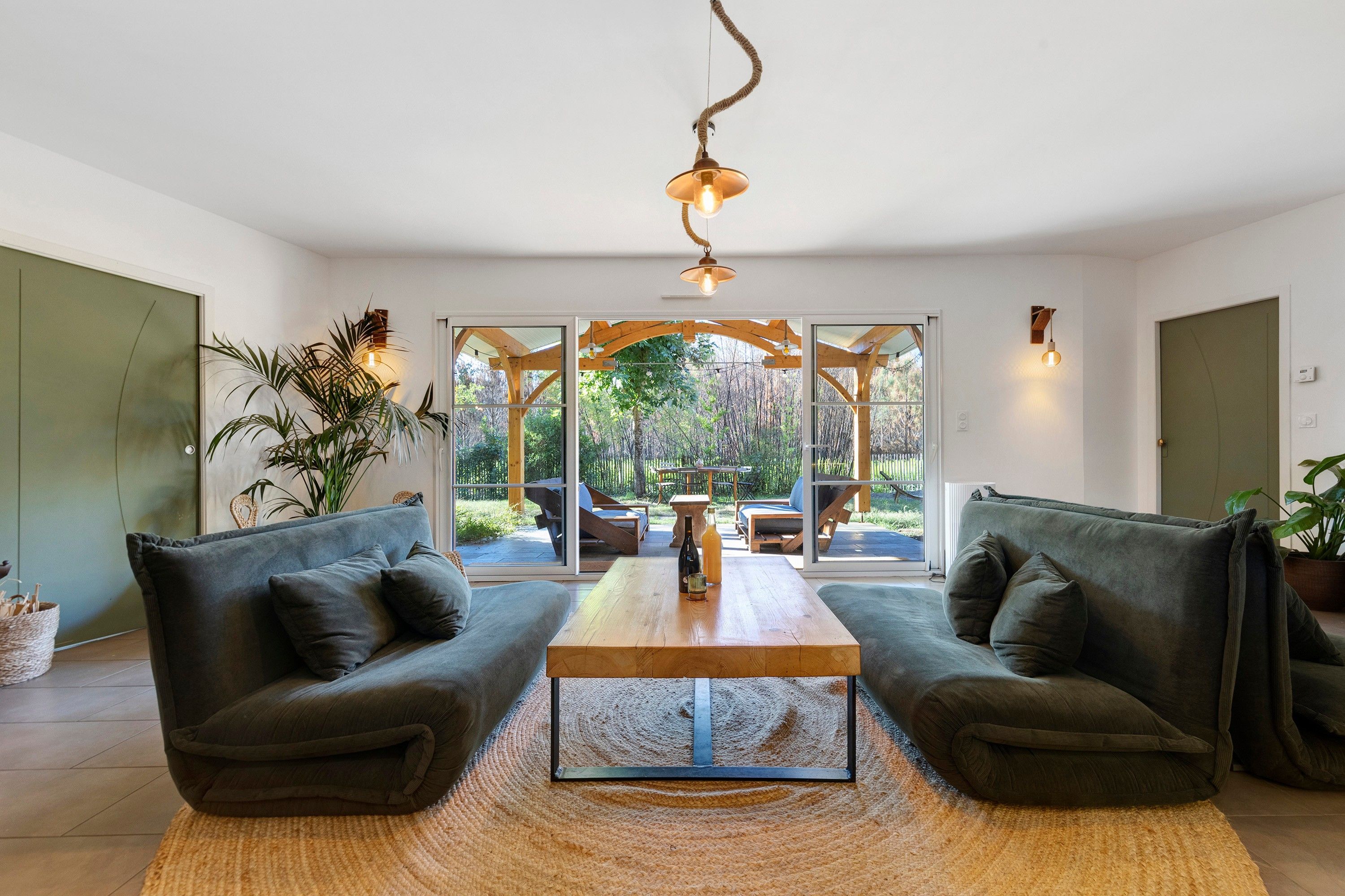 Ein modernes Wohnzimmer mit einer Sofagarnitur, einem Couchtisch und Blick ins Freie durch große Glasfenster.