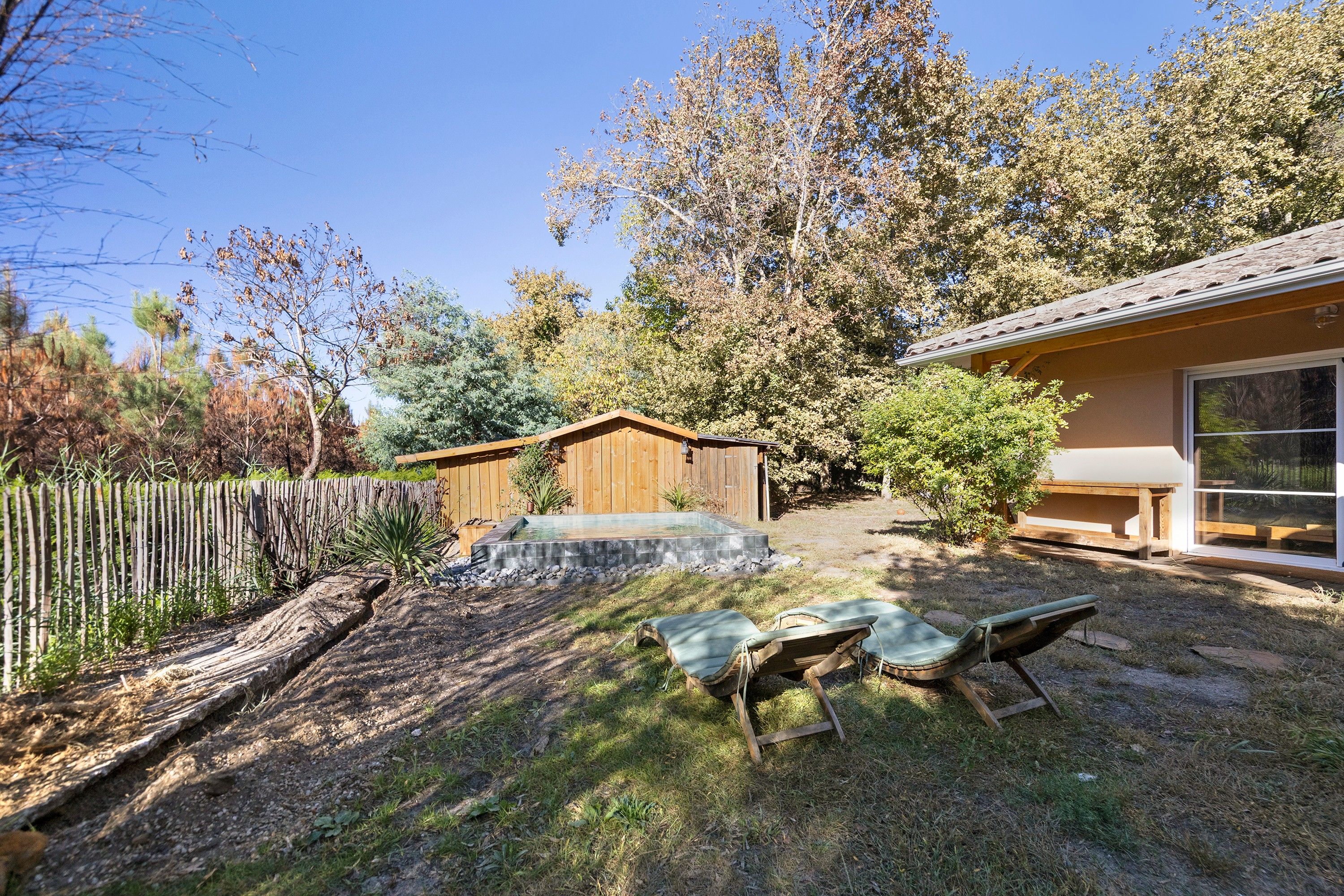 A backyard with a wooden deck, two lounge chairs, a hot tub, and a wooden fence.