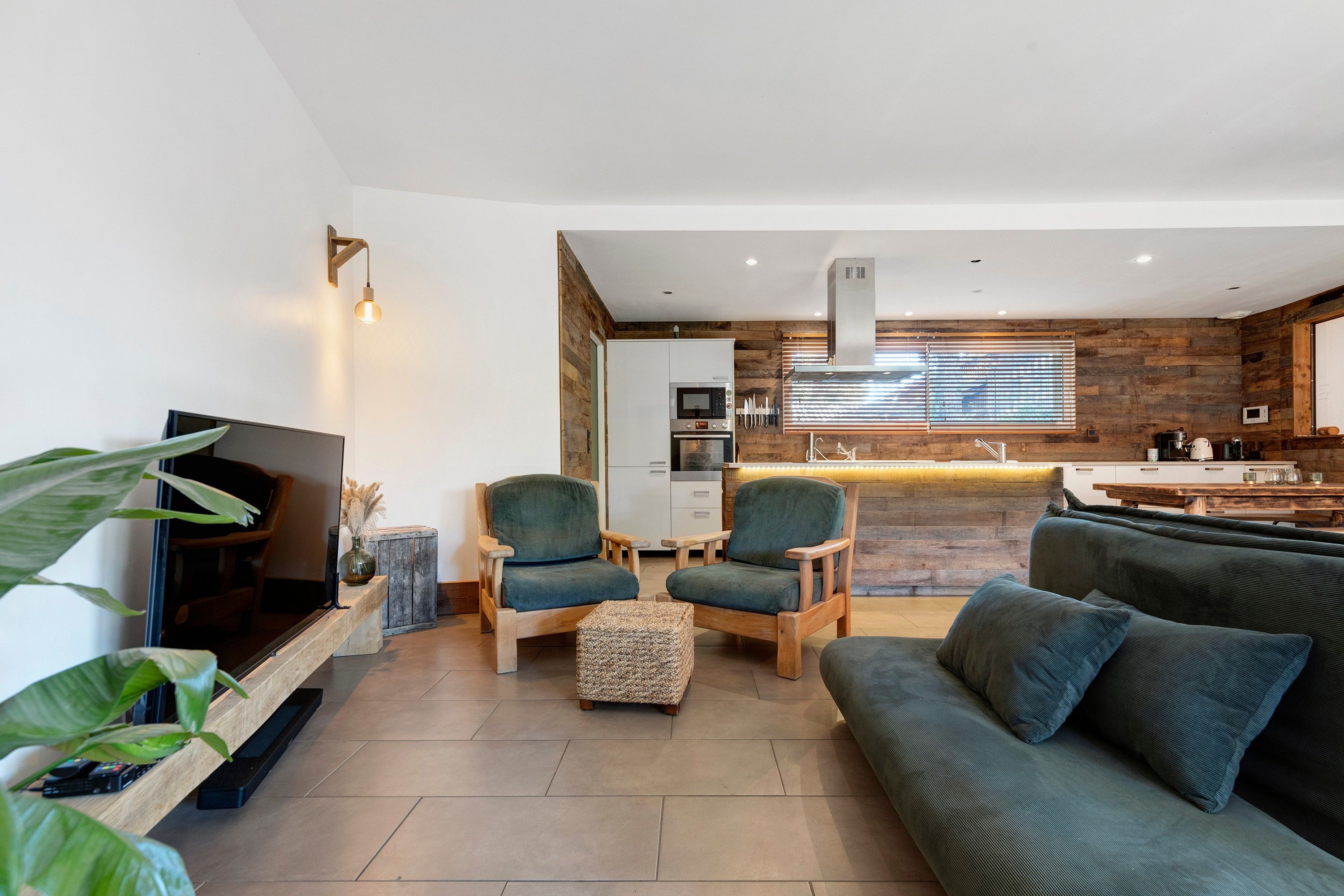 A modern living room with a television, seating area, and a kitchen in the background.