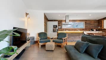 A modern living room with a television, seating area, and a kitchen in the background.