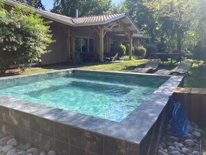 Piscina rectangular con agua cristalina, rodeada por un deck de baldosas y un deck de madera con sillones de descanso.