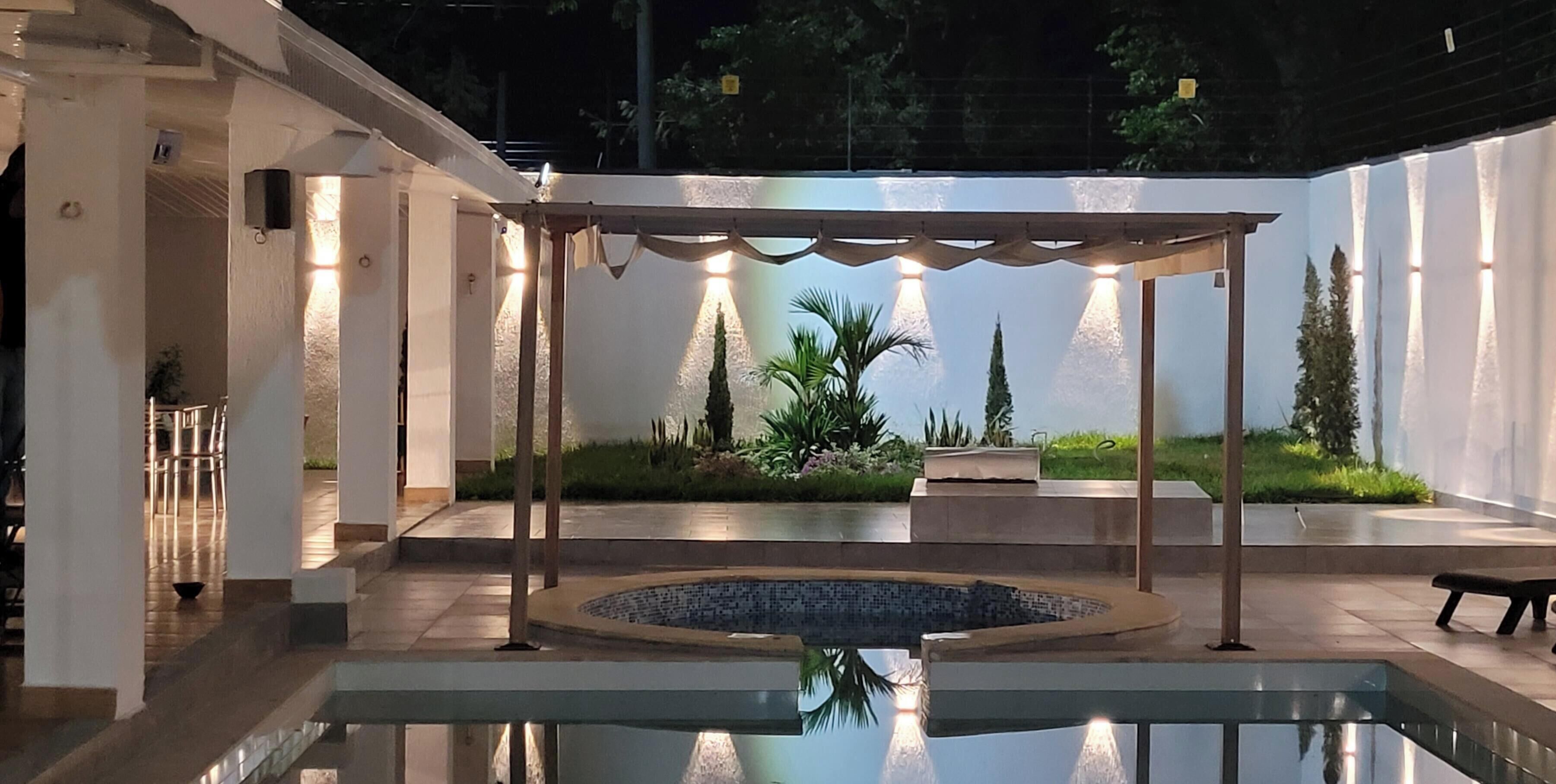 A pool area with a circular water feature, surrounded by a covered seating area and plants.