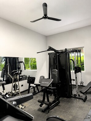 A gym with exercise equipment, a ceiling fan, and windows with a view of greenery. - Area 89. Stunning Villa—Pool, Hot Tub, and Home Theater, Just 5 Minutes from the Hot Springs (Rivera)