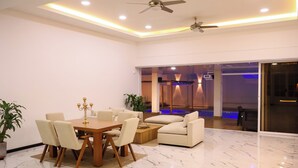 A modern living room with a dining area, featuring a marble floor, a ceiling fan, and a large window.