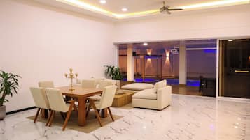 A modern living room with a dining area, featuring a marble floor, a ceiling fan, and a large window.