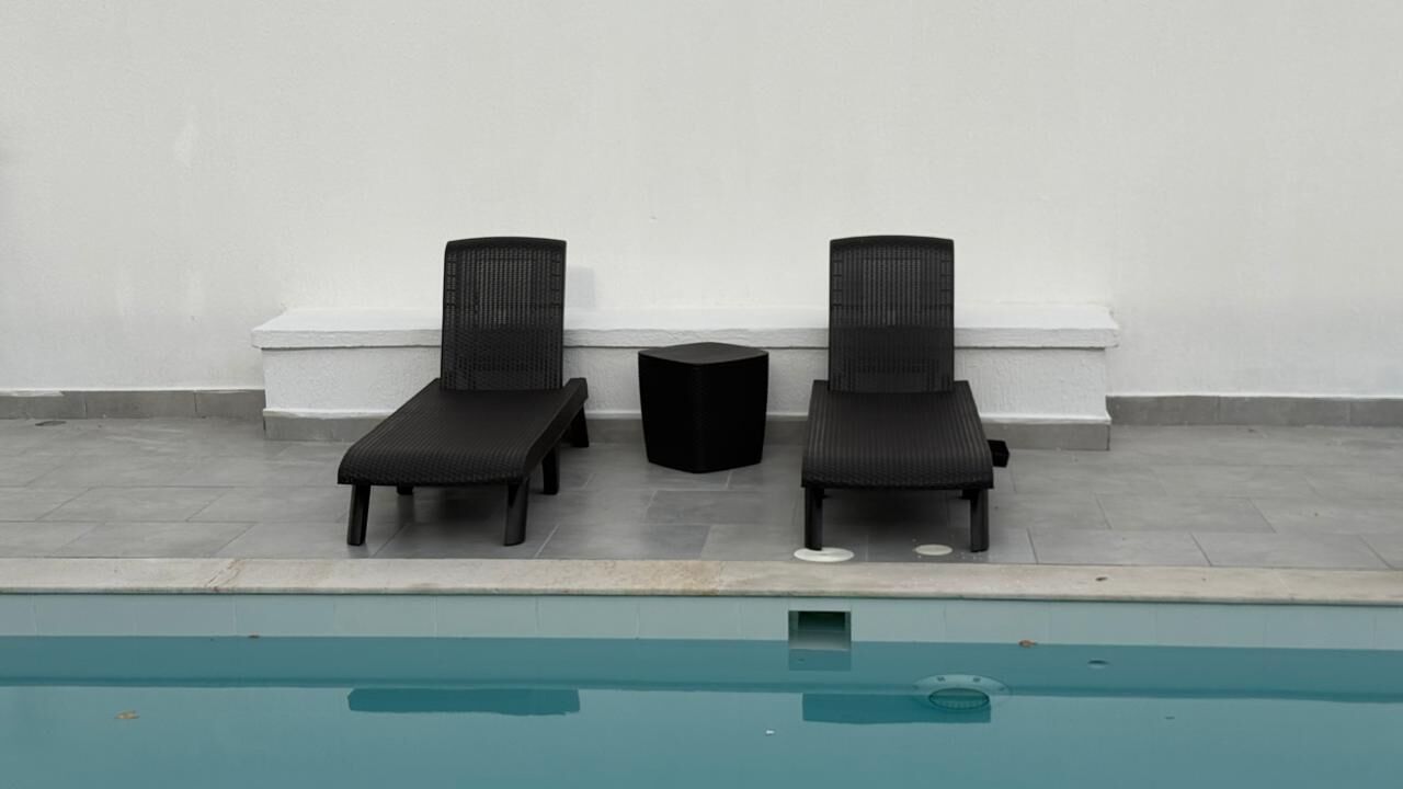 Dos sillones de descanso y una mesita junto a una piscina.
