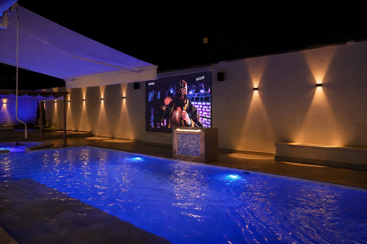 Une piscine éclairée de lumières bleues, un grand écran diffusant un film et des lampes fixées aux murs.