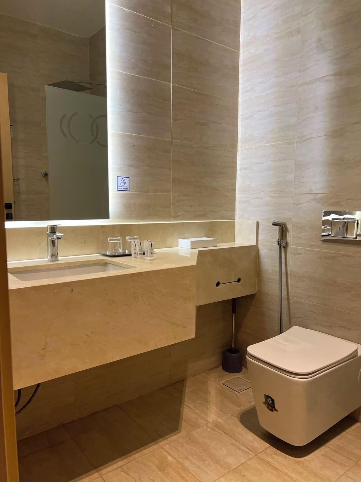 A modern bathroom with a large mirror, a sink with a faucet, a toilet, and a handheld showerhead.
