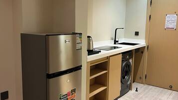 A compact kitchen with a stainless steel refrigerator, a washing machine, and a sink.