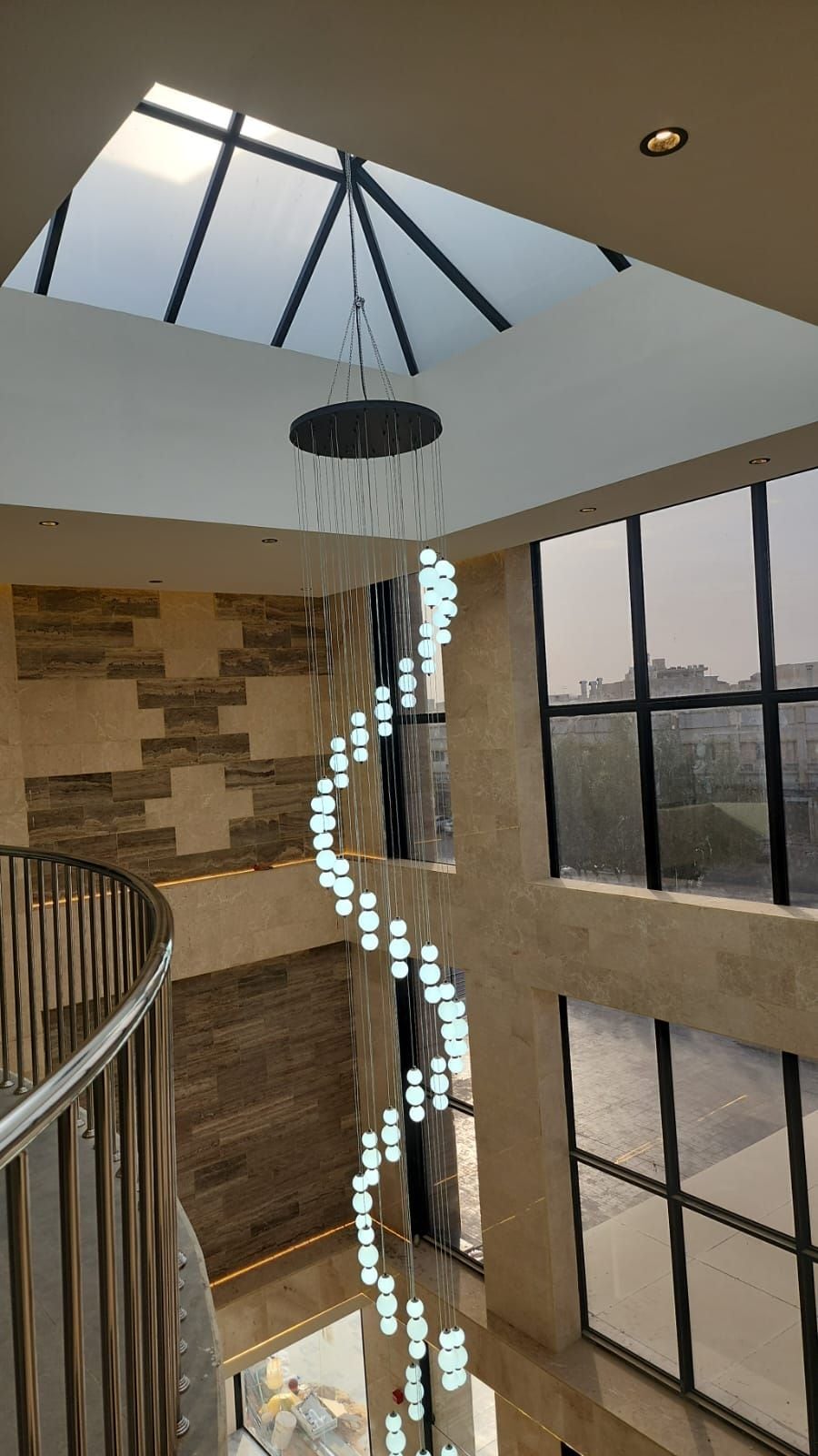 A modern interior with a skylight, a hanging light fixture, and a view through large windows.
