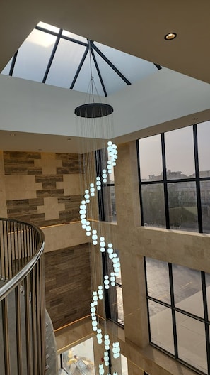 A modern interior with a skylight, a hanging light fixture, and a view through large windows. - Best western centria (Riyadh)
