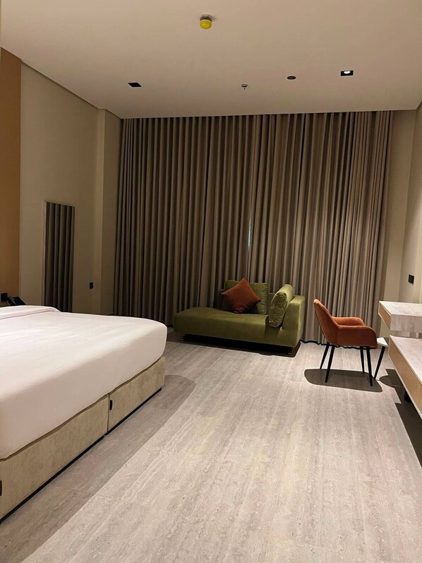 A modern hotel room with a large bed, a green sofa, a small orange chair, and a desk. - Best western centria (Riyadh)