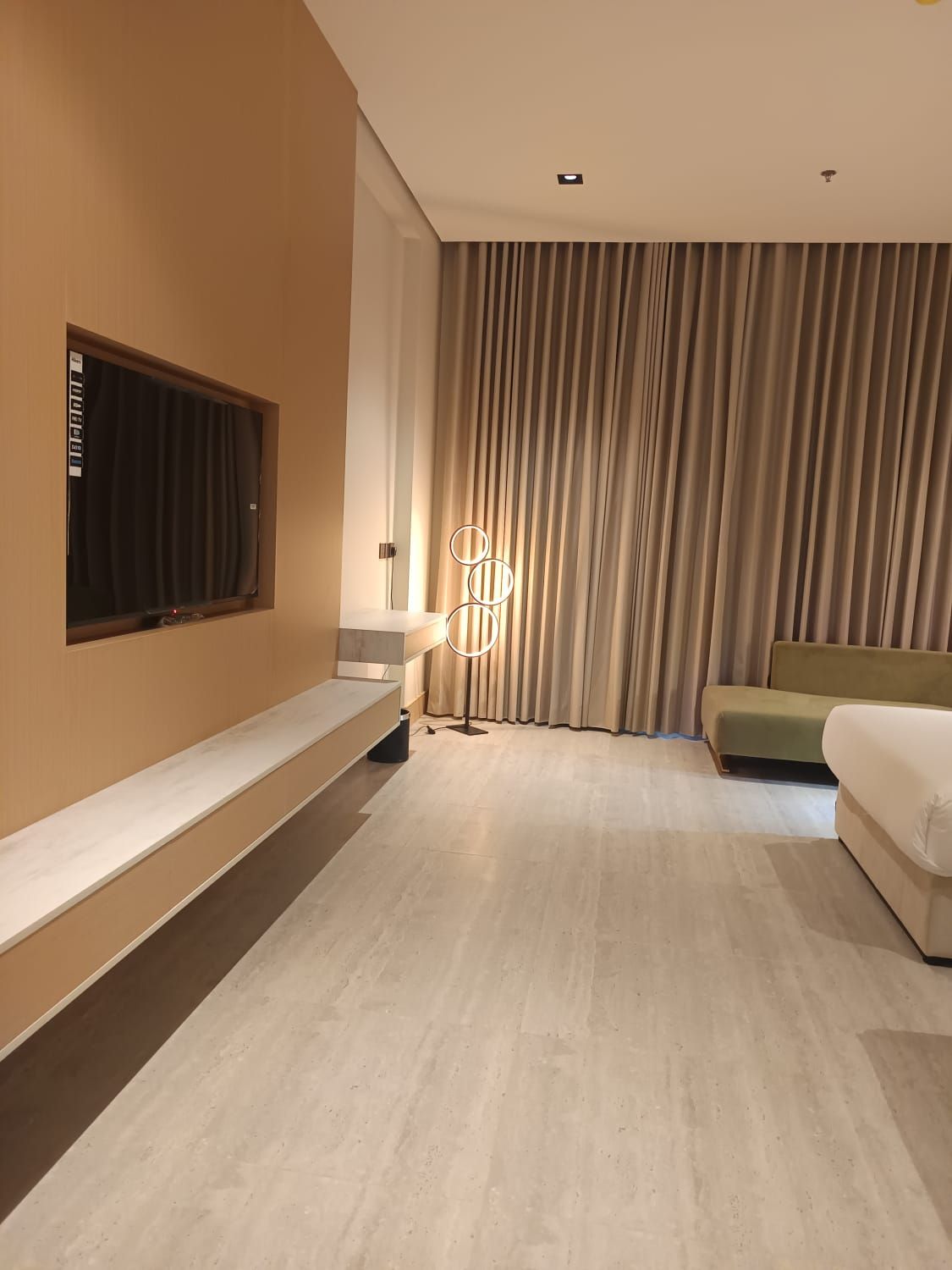 Una habitación de hotel moderna con un ventanal grande, un televisor de pantalla plana, un sofá, una mesita de noche y una lámpara de pie.