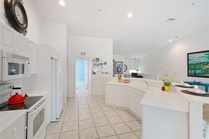 A modern kitchen with white cabinetry, a red kettle, a microwave, and a large window. - Turnkey 3BR/2BA Seasonal Rental - Gated Community Palm Grove at Tara Preserve (Bradenton)