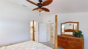 Ein Schlafzimmer mit Himmelbett, einem Holzkommode mit Spiegel und Deckenventilator.