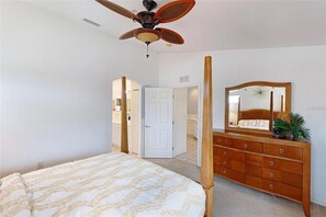 Ein Schlafzimmer mit Himmelbett, einem Holzkommode mit Spiegel und Deckenventilator.