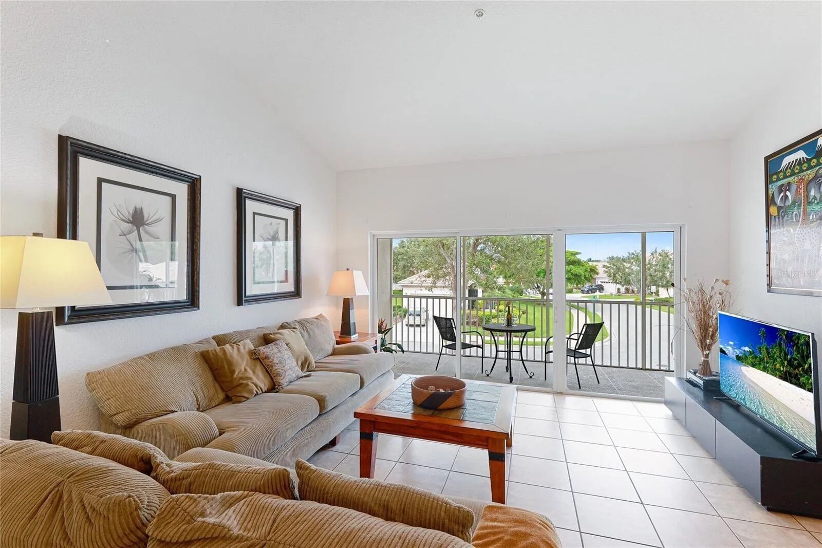 A living room with a sofa, a coffee table, a TV, and a balcony with outdoor furniture.