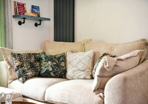 A beige sofa with patterned cushions, a dark vertical panel, and a shelf with books. - Modern 2BR Cardiff Home | 2 Bath, Close to Centre - Pass the Keys (Cardiff)