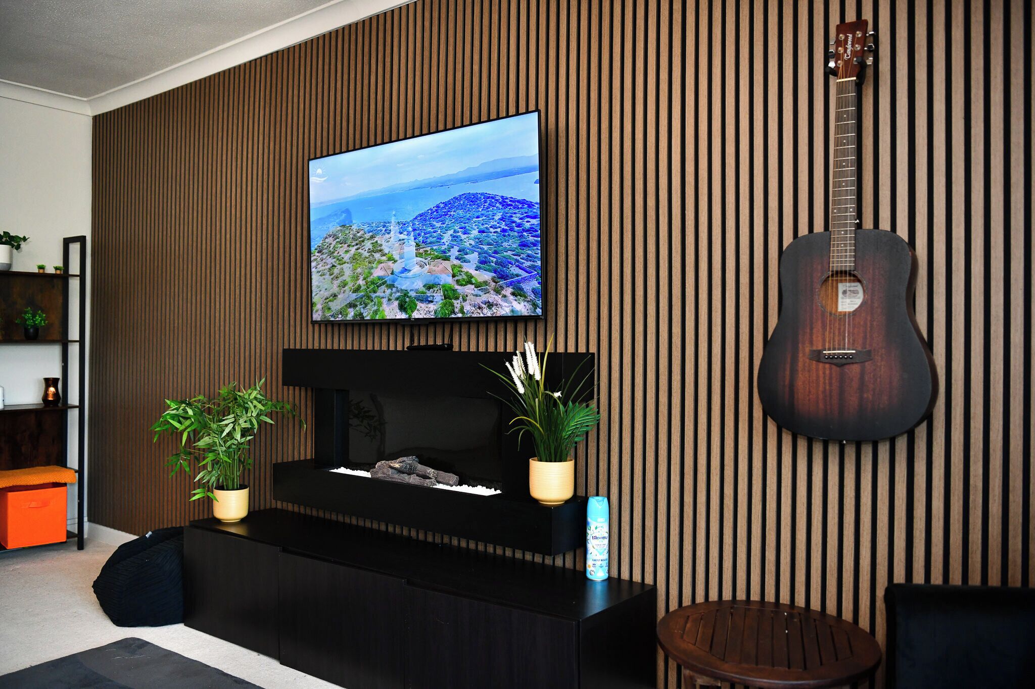 A living room with a television, a guitar, and a fireplace.