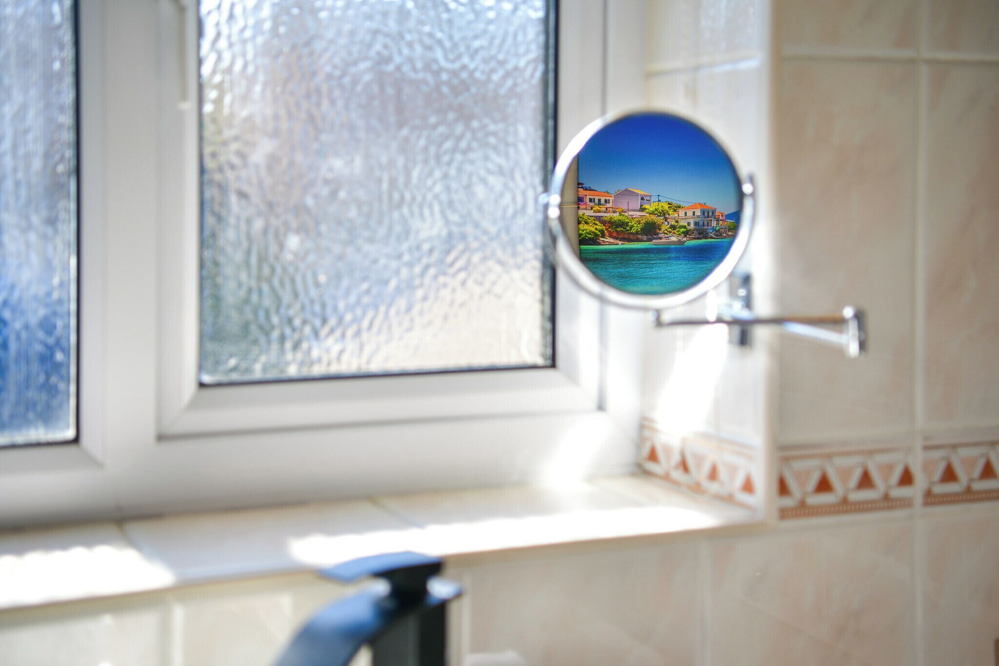Ein Badezimmer mit einem satinierten Fenster, einem runden Spiegel und einer gefliesten Wand.