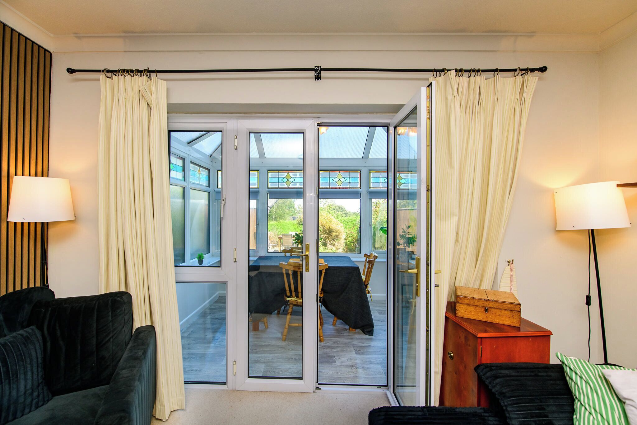 A room with a sliding glass door leading to an outdoor area, a dark-colored sofa, a wooden cabinet, and a lamp.