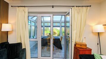 A room with a sliding glass door leading to an outdoor area, a dark-colored sofa, a wooden cabinet, and a lamp.