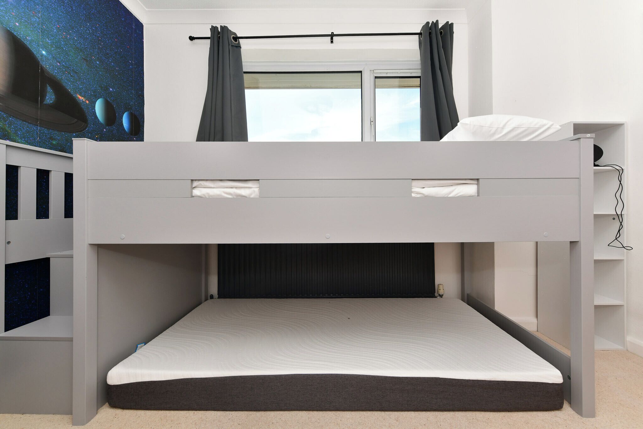 A bunk bed with a pull-out desk and a night sky mural on the wall.