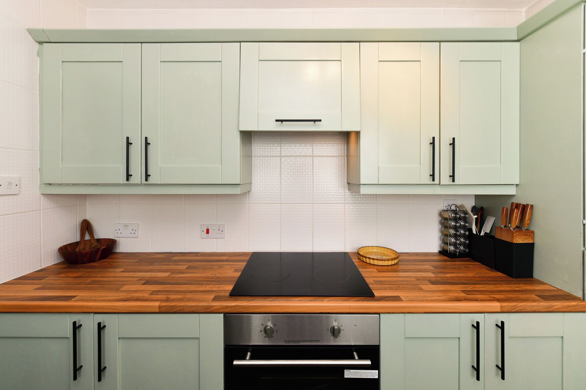 A kitchen with light green cabinets, a wooden countertop, and a built-in oven.