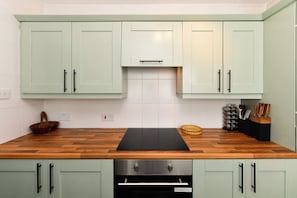 A kitchen with light green cabinets, a wooden countertop, and a built-in oven.