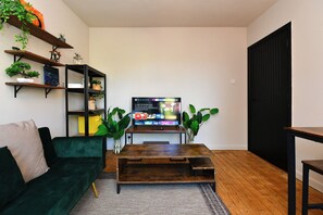 Ein Wohnzimmer mit einer Couch, einem Couchtisch, einem Fernseher und Regalen mit Pflanzen.
