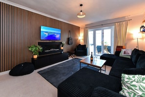 A modern living room with a flat-screen TV, a piano, a sofa, a coffee table, and a view through a glass door.