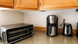 Uma cozinha com armários de madeira, forno elétrico, cafeteira e chaleira.