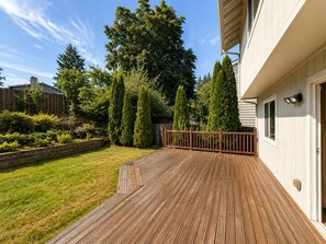 A wooden deck with a railing, a grassy lawn, and a variety of trees. - Quiet Renton 3BR House near Valley Medical Ctr (Renton)