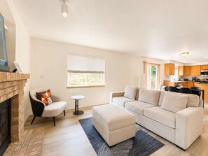 A modern living room with a fireplace, sofa, ottoman, and a small round table. - Quiet Renton 3BR House near Valley Medical Ctr (Renton)