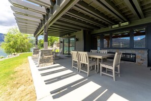 Eine Außenpatio mit Kamin aus Stein, einem Esstisch mit Stühlen und einer Pergola darüber.