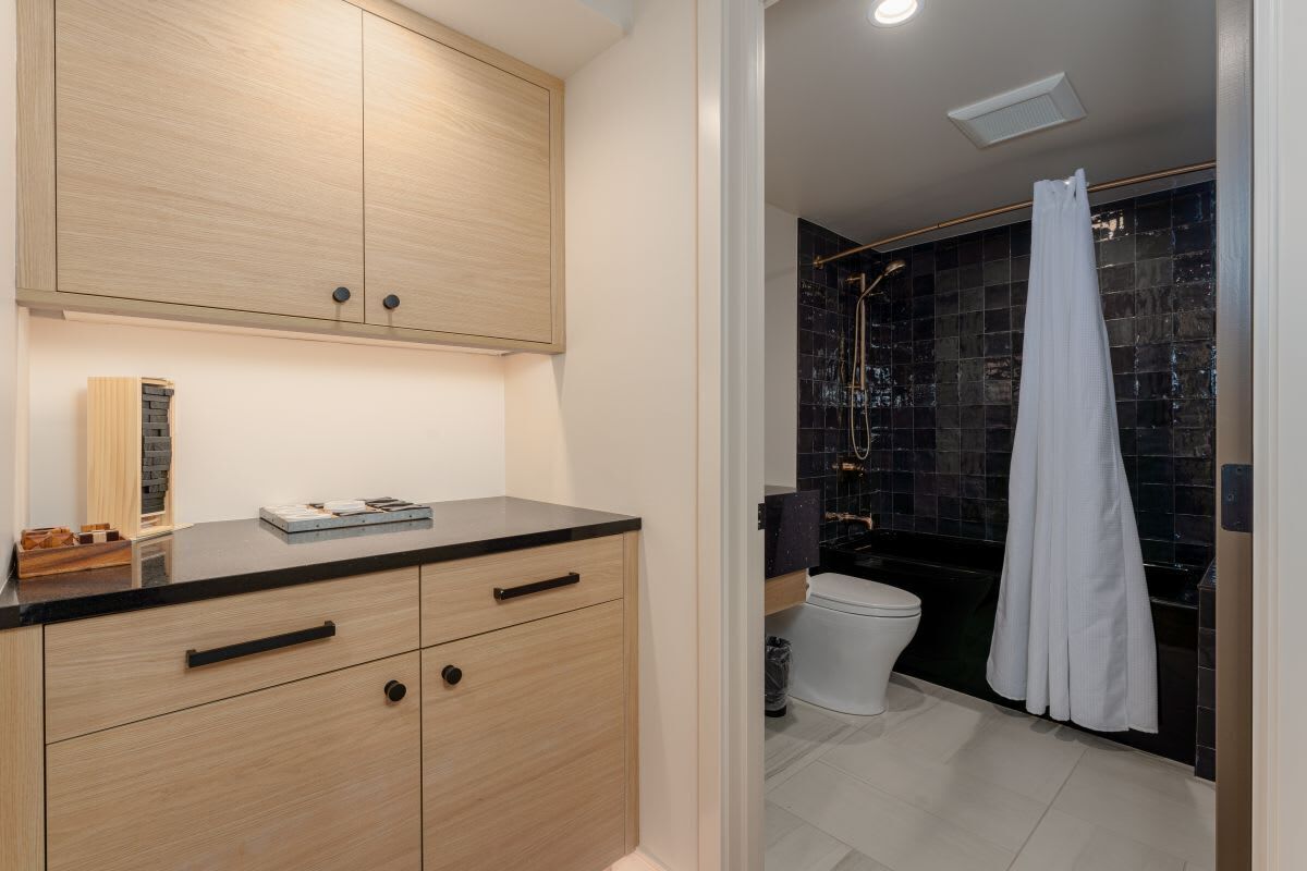 A modern bathroom with a wooden vanity, a shower with a black tiled wall, and a white toilet.