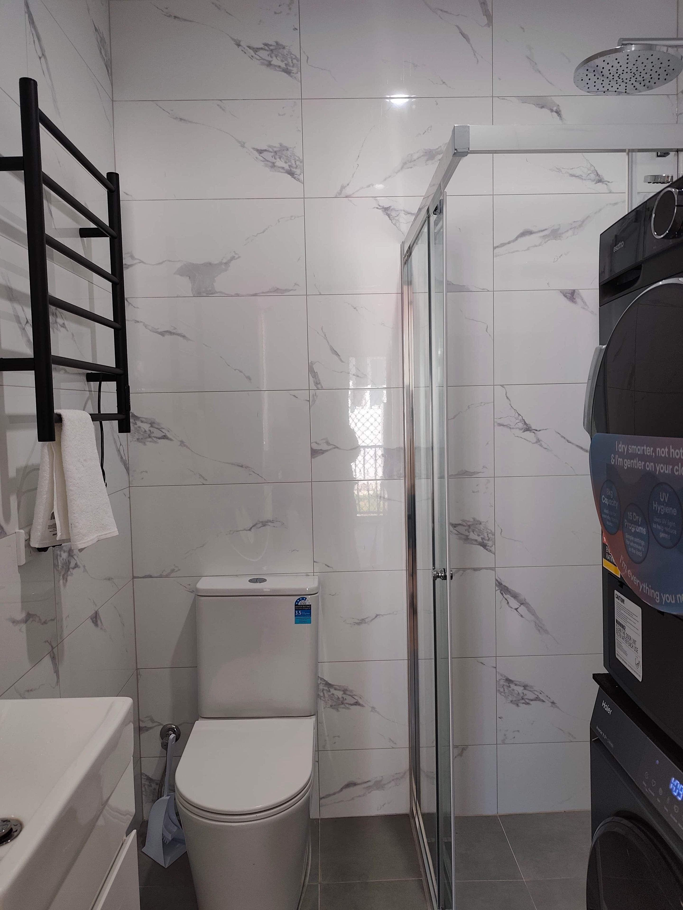 A modern bathroom with a toilet, a shower enclosure, and a towel rack.