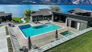 Ein modernes Wohnhaus mit großem Pool, überdachter Terrasse und Blick auf einen See und Berge.