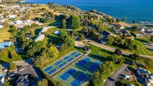 Eine Vogelperspektive auf ein Wohngebiet mit mehreren Tennisplätzen, einem Schwimmbad und einem See im Hintergrund.