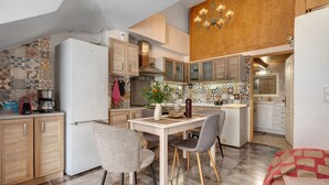 Une cuisine moderne avec un coin repas, des meubles en bois, un réfrigérateur blanc et un lustre.