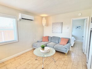 Ein modernes Wohnzimmer mit einem grauen Sofa, einem Glastisch und einer Zimmerpflanze.