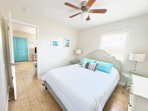 Een slaapkamer met een bed, een plafondventilator, een raam met jaloezieën en een deur naar een andere kamer.