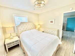 Ein Schlafzimmer mit einem großen Bett, Nachttischlampen, einem Schminktisch und einer Tür zu einem weiteren Raum.