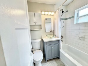 Ein Badezimmer mit Toilette, einem Waschtisch mit Glasbecken, einer Dusche mit Duschbrause und einer Badewanne.