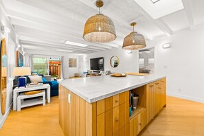 Een moderne keuken met een centraal eiland, houten keukenkastjes en twee hangende wilgentrootjeslampen.