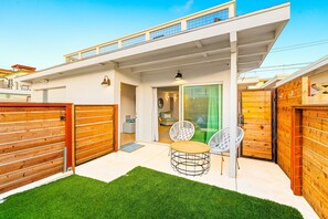 Ein modernes Haus mit einer überdachten Terrasse, einem Holzzaun und einem grünen Rasen.