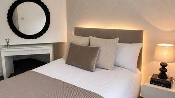 Une chambre d’hôtel avec un grand lit, une table de chevet avec une lampe, un miroir rond et un lustre.